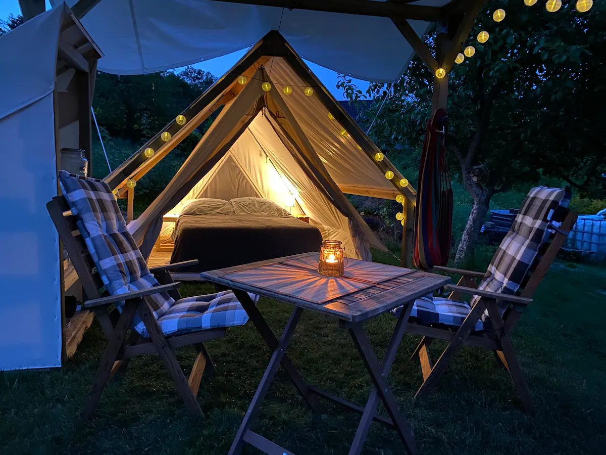 Glamping-Zelt mit gedecktem Tisch und Lichterkette am Abend